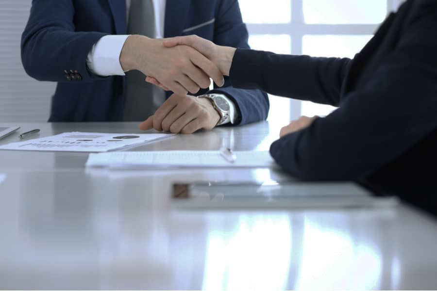 Close-up of lawyer in suit shaking hands with client while sitting at a table.