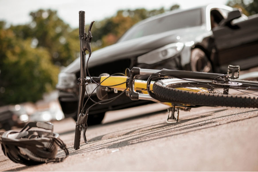 Close-up of a yellow bicycle on its side on the road with a helmet sitting next to it with a car in the background.