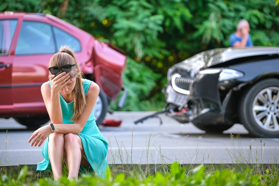 Woman sitting on the side of a road with her head in her hands with an auto accident in the background