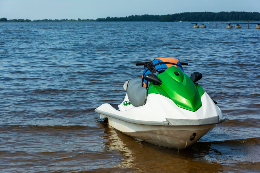 A green jetski on the sand in shallow water on the edge of a lake.